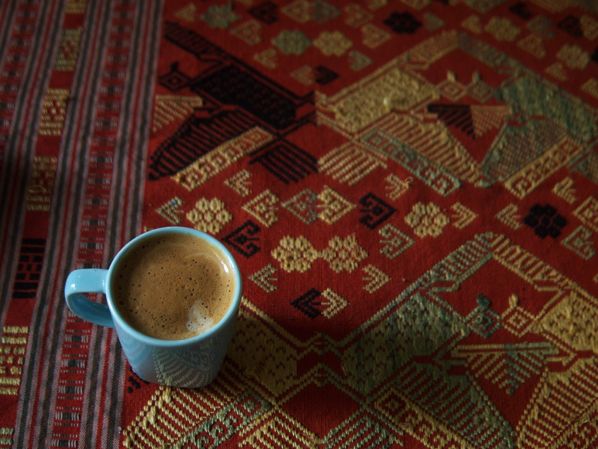 A small cup of coffee with milk on a woven red and gold cloth