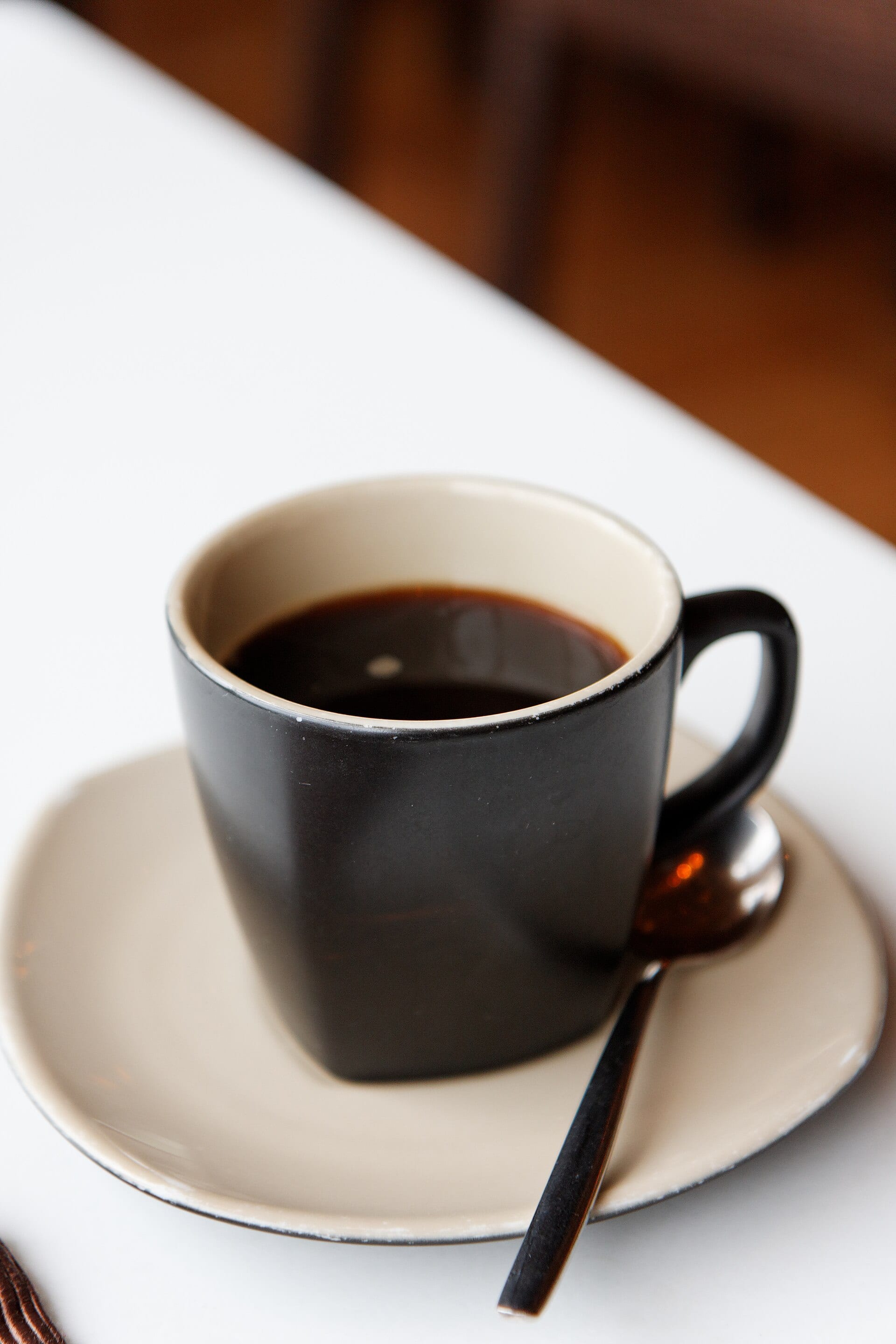 A cup of black coffee on a saucer with a spoon