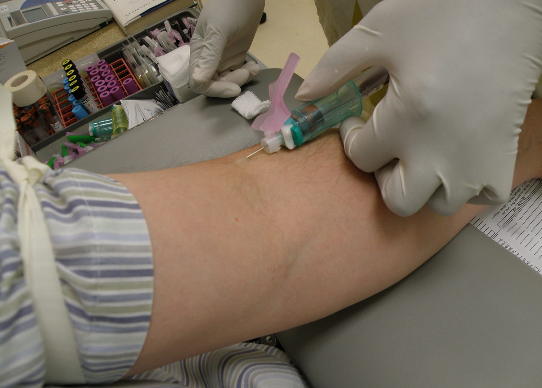 A blood draw from a forearm, with collection tubes on the tray behind