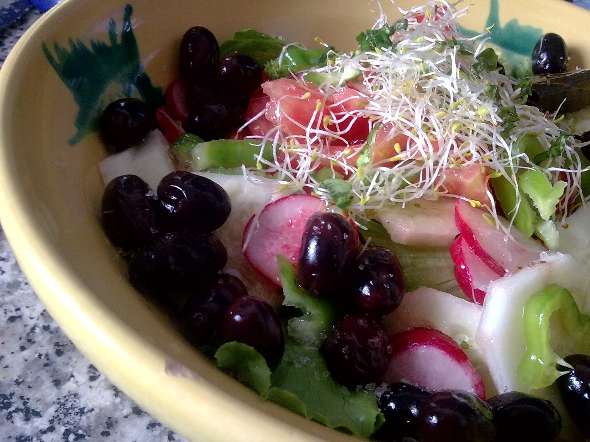 Salad with olives, radish and sprouts dressed in olive oil