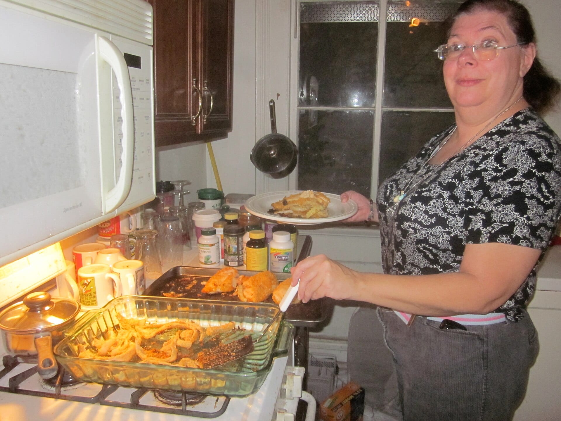 A woman serving dinner from a baking dish in a home kitchen