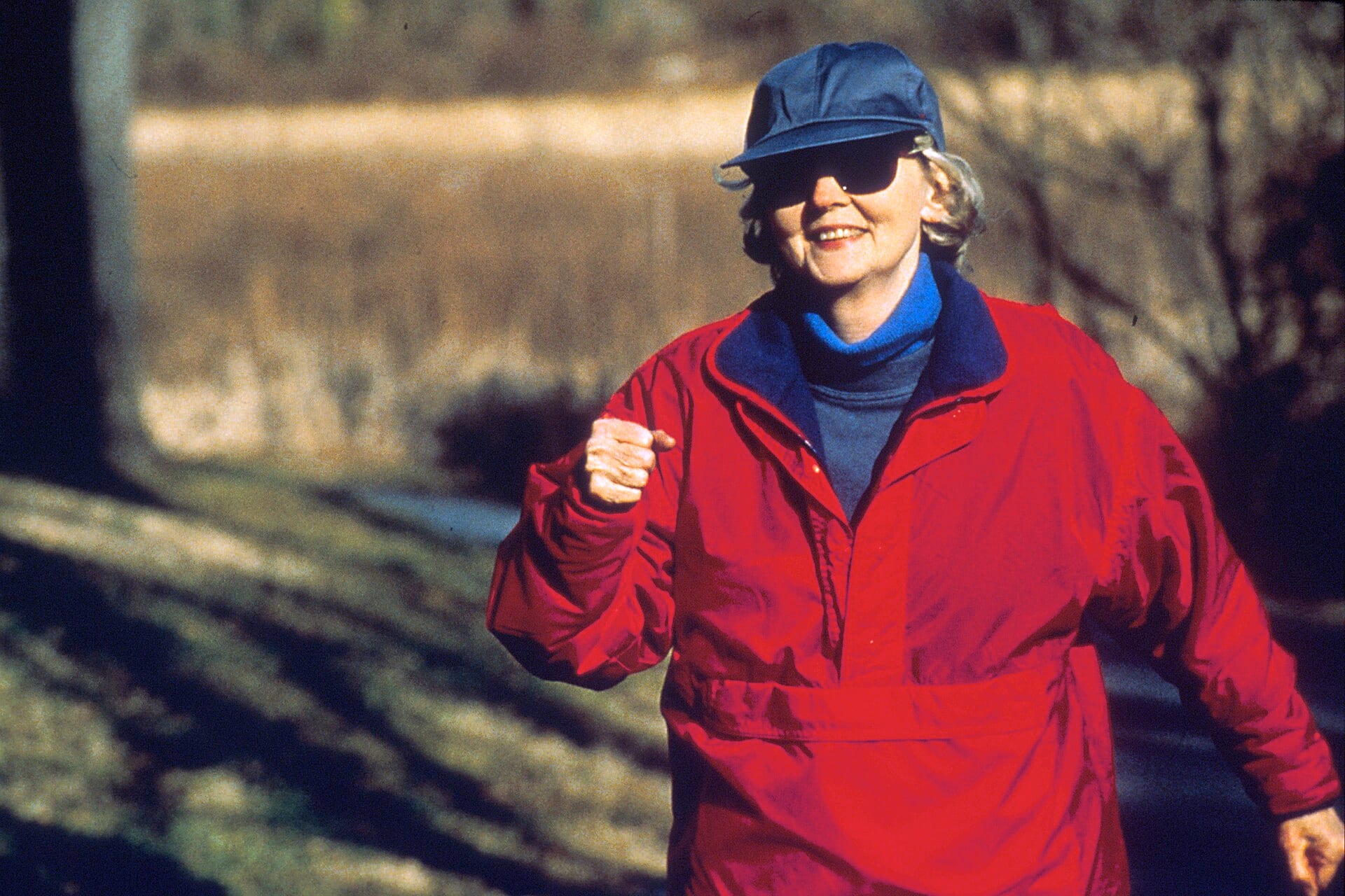 An older woman in a red jacket and cap walking briskly outdoors