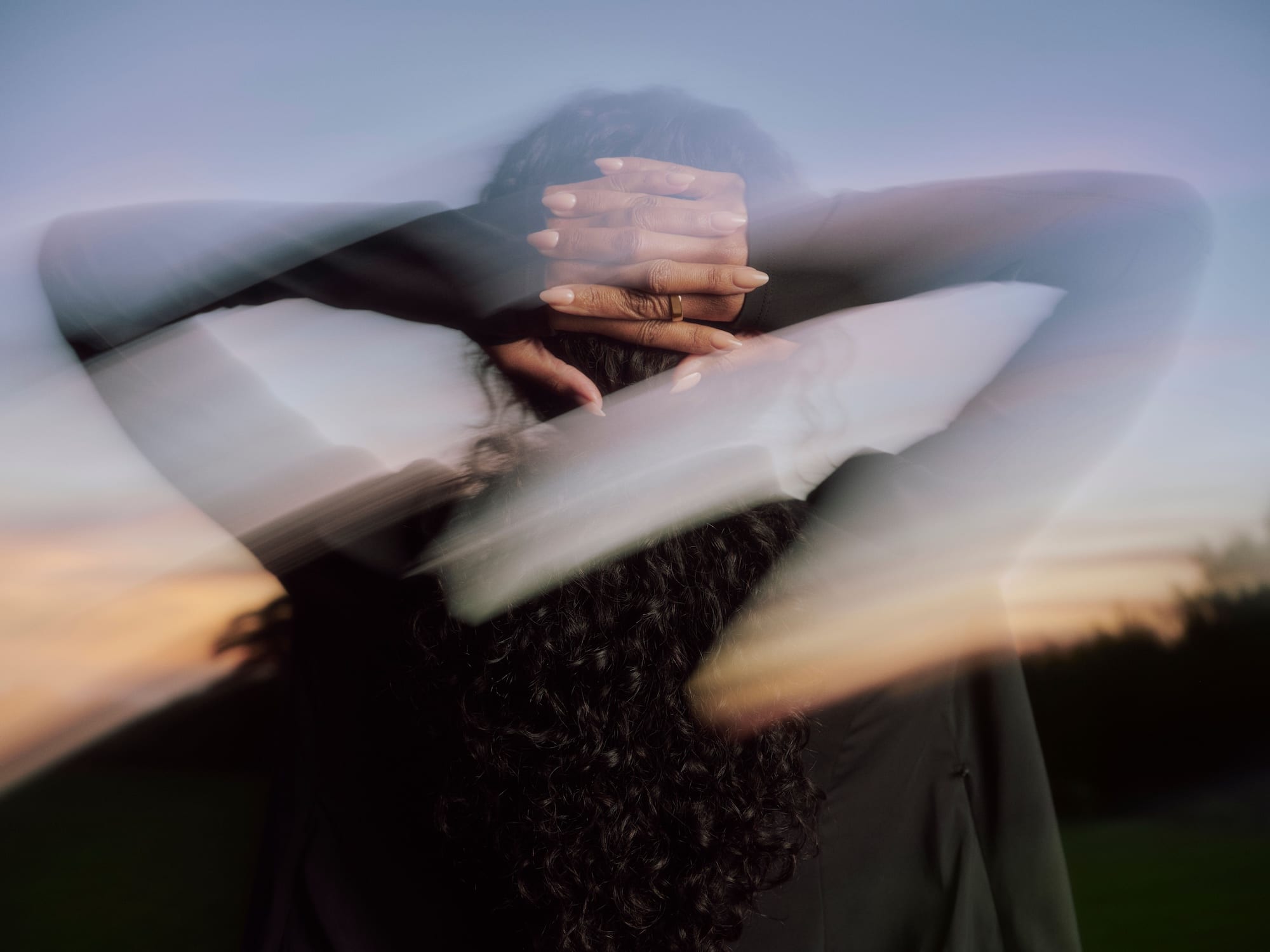 A person stretching outdoors at dusk, arms raised behind the head