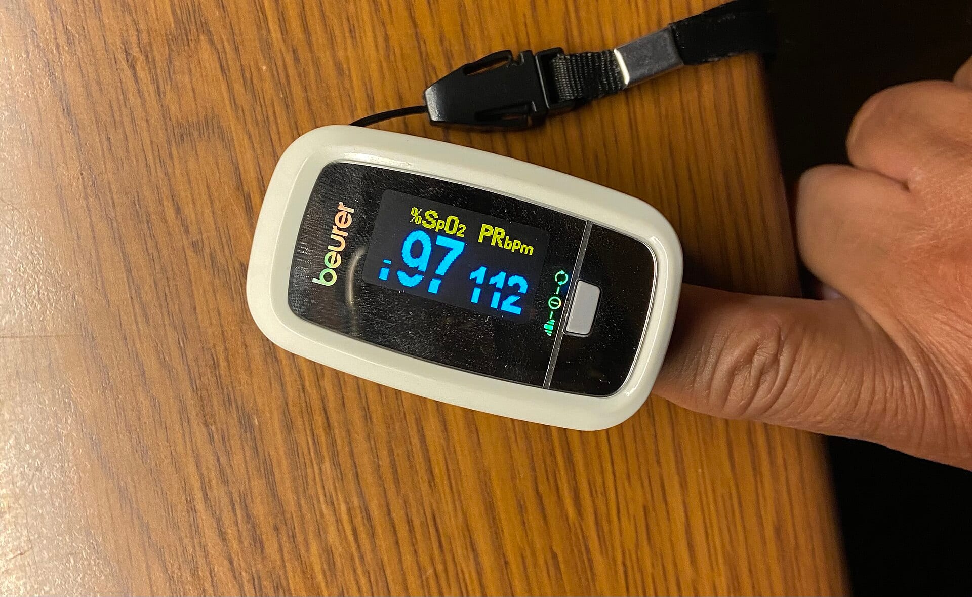 A fingertip pulse oximeter clipped on a finger, showing an oxygen saturation of 97 and a pulse of 112